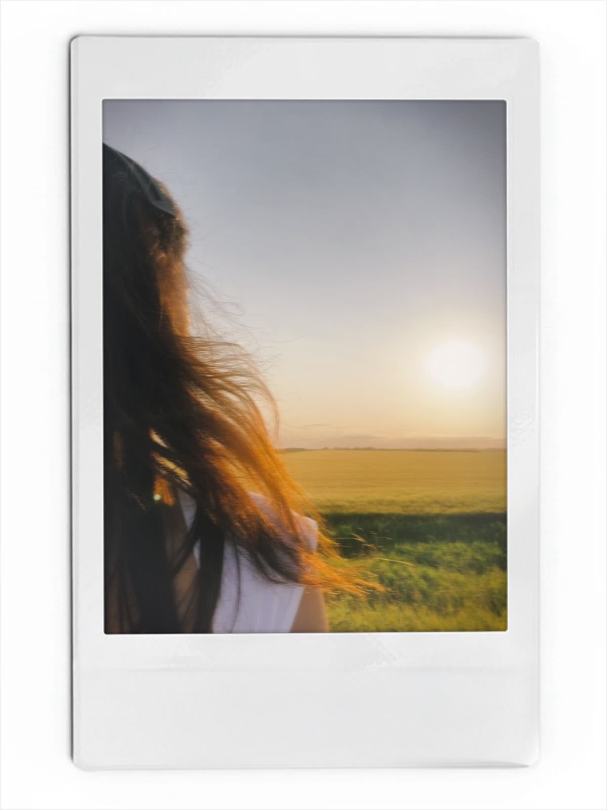 An instant-film photograph of a woman looking out over a field at sunset.