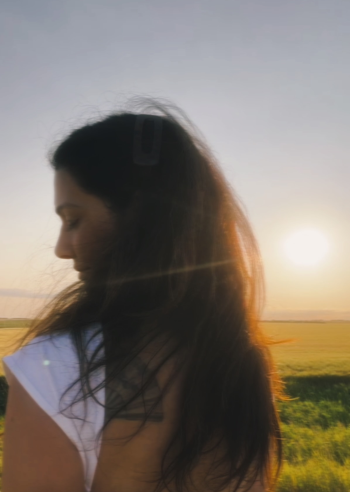 A woman turned away from the camera in a prairie field, backlit by a low sun.